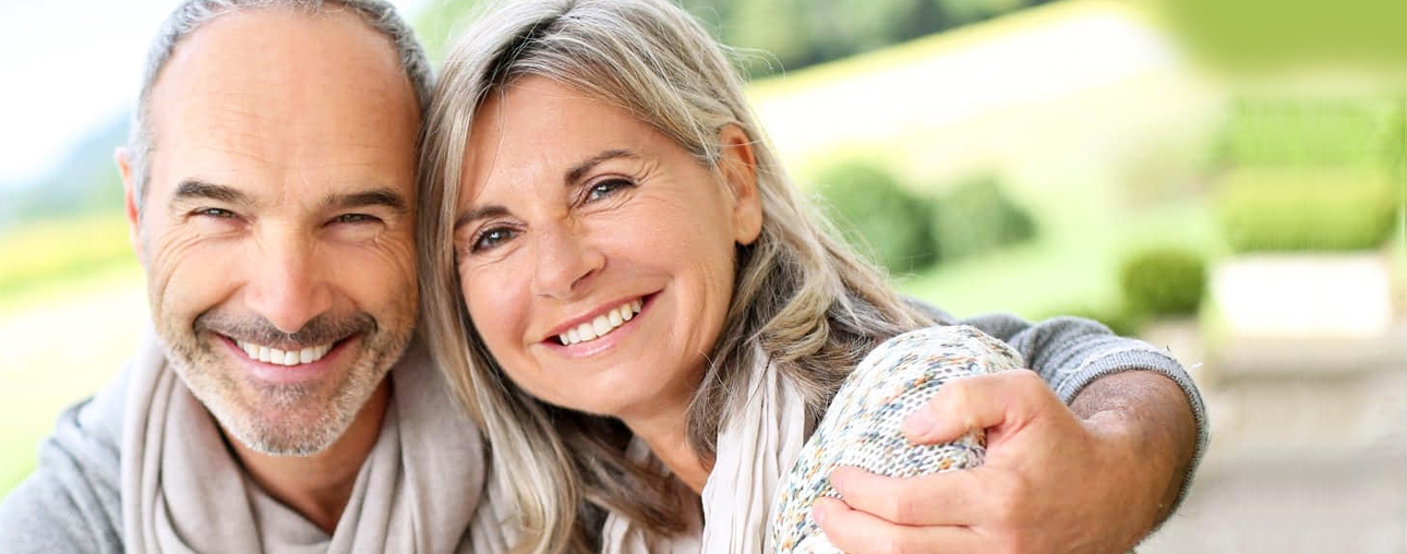 Happy mature couple smiling outdoors in garden setting, embracing each other warmly.