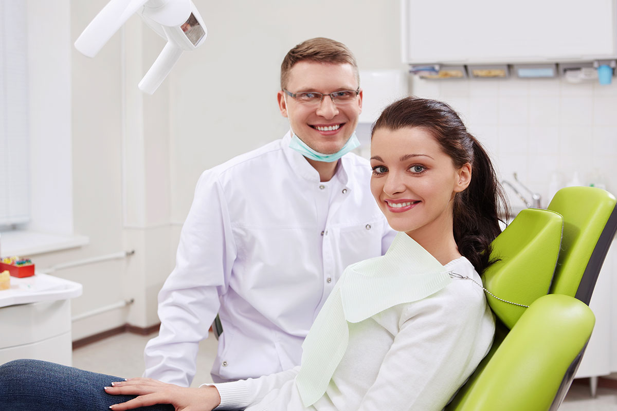 Smiling dentist and female patient in bright dental office chair during consultation.
