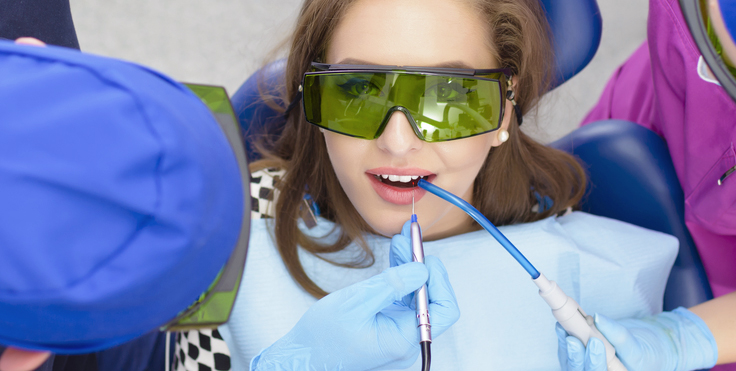 Young girl wearing protective eyewear receiving dental treatment from dentist in blue gloves.