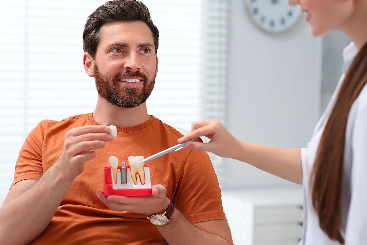 Dentist showing patient dental implant model in bright office setting.