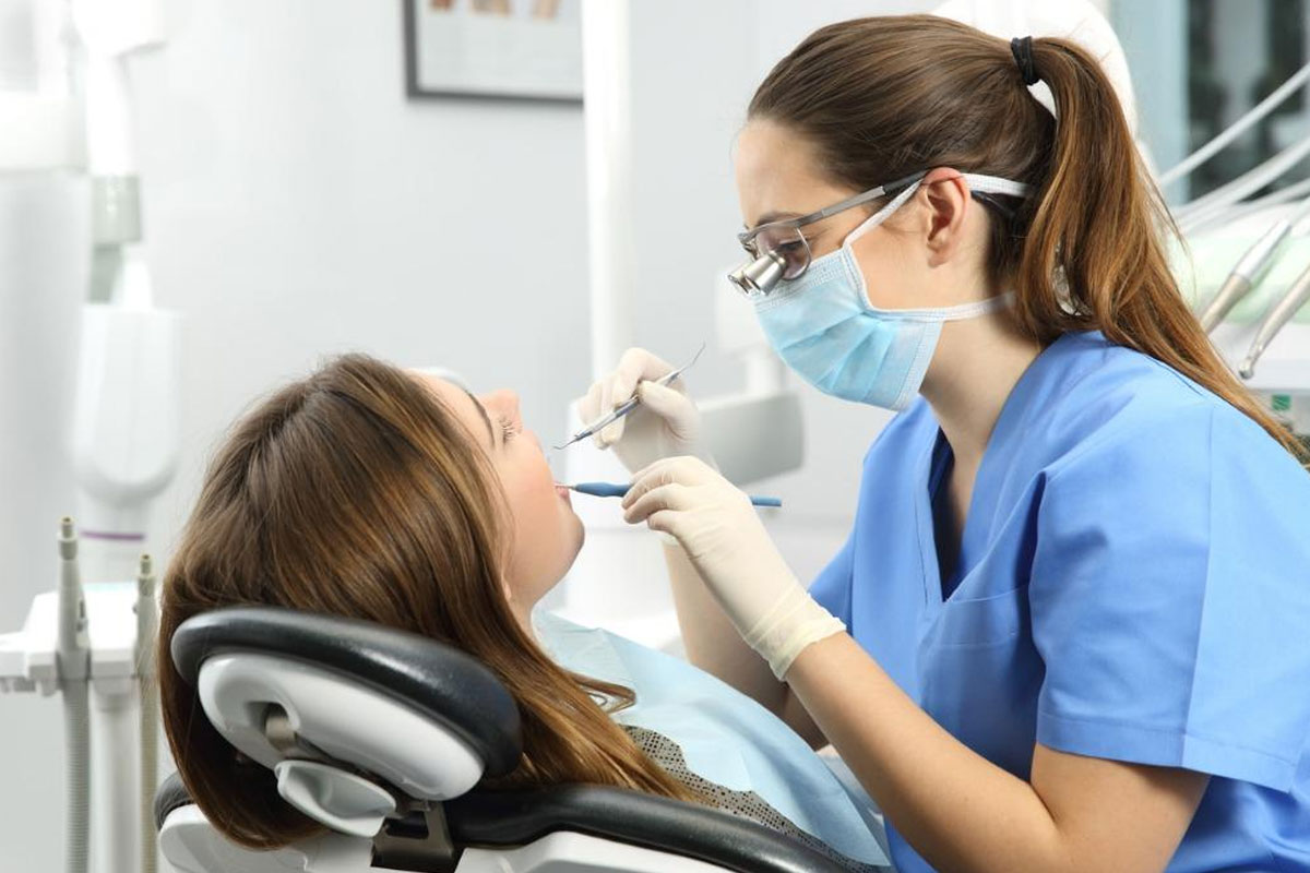 Dentist examining patient's teeth in modern dental clinic wearing protective mask and eyewear.