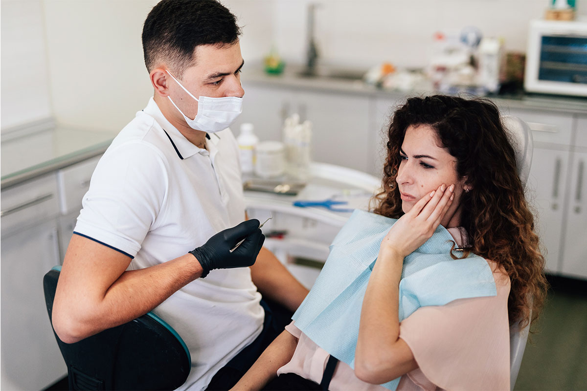 Dentist in white coat and mask examining patient in dental office setting.
