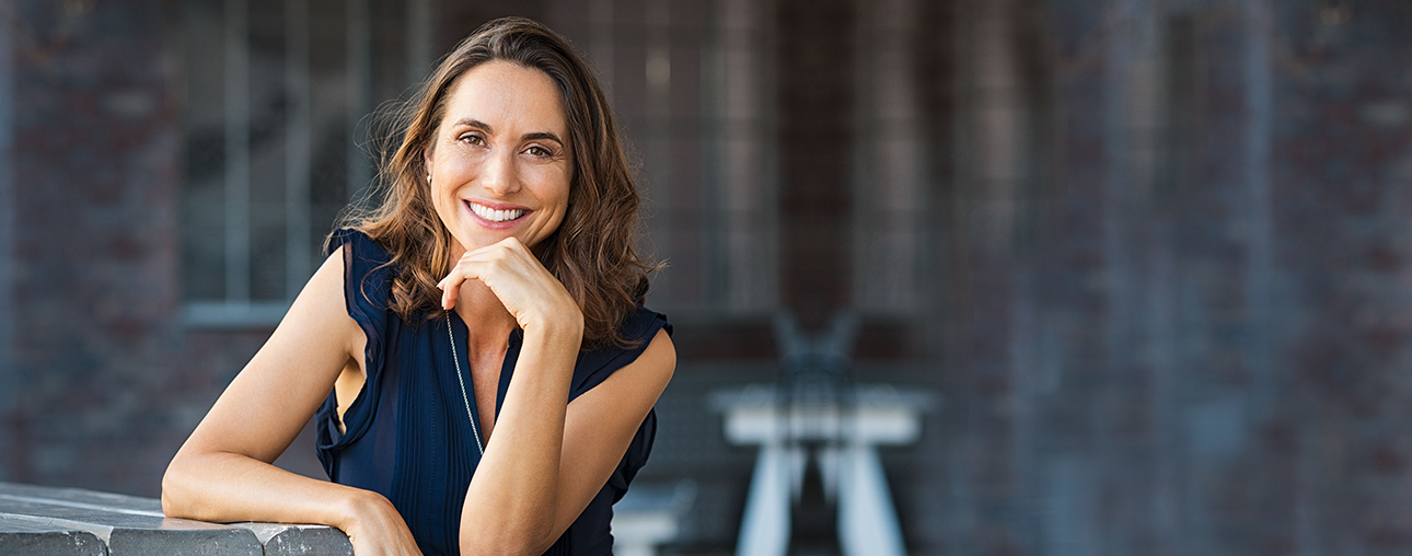 Professional woman smiling at camera in navy blouse against urban brick building backdrop.