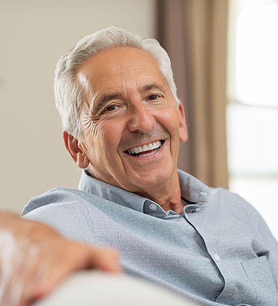 Smiling senior man in light blue shirt relaxing indoors near window