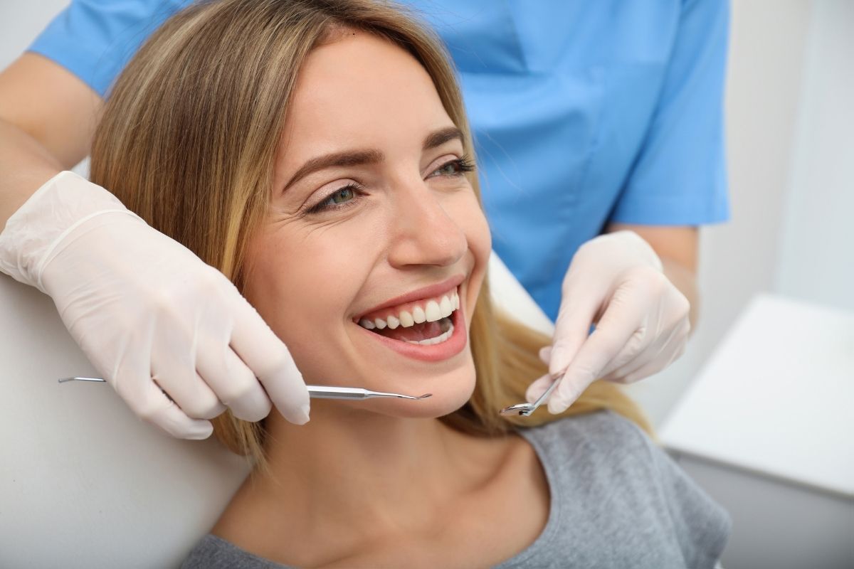 Woman smiling during dental examination with dentist holding instruments in clinical setting.