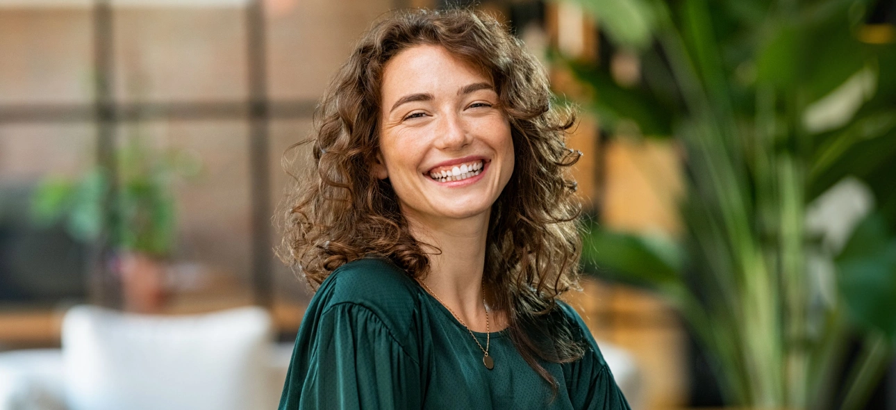 Smiling woman in green shirt at dental office with plants in background