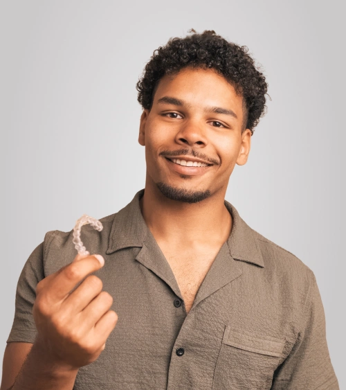 Smiling man in brown shirt giving thumbs up gesture against neutral background.